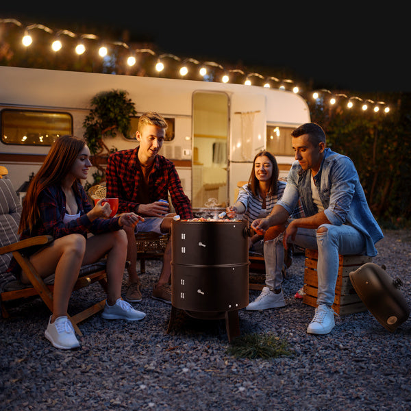 Group of friends around a black smoked charcoal oven, grilling food at a campsite.